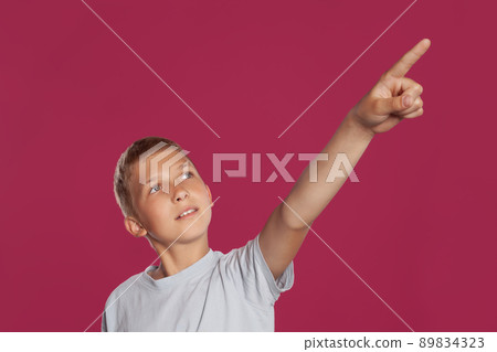 Close-up portrait of a blonde teenage boy in a white t-shirt posing against a pink studio background. Concept of sincere emotions. 89834323