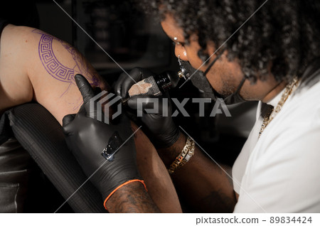 Professional African American tattoo artist makes a tattoo on client arm Professional African American tattoo artist makes a tattoo on client arm 89834424
