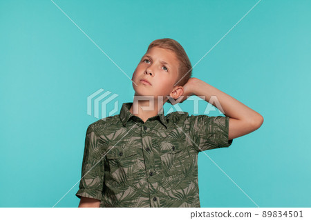 Close-up portrait of a blonde teenage boy in a green shirt with palm print posing against a blue studio background. Concept of sincere emotions. 89834501