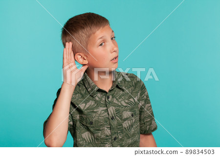 Close-up portrait of a blonde teenage boy in a green shirt with palm print posing against a blue studio background. Concept of sincere emotions. 89834503