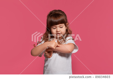 Close-up portrait of a little brunette girl dressed in a white t-shirt posing against a pink studio background. Sincere emotions concept. 89834603