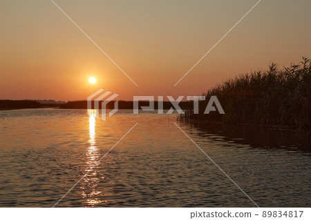 Sunset over a calm lake, water wave reflection 89834817