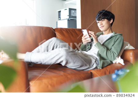 A young man lying on the sofa at home and touching his smartphone A young man lying on the sofa at home and touching his smartphone 89834924
