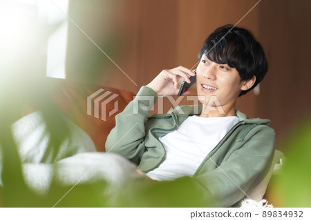 一個年輕人躺在家裡的沙發上，用智能手機說話 89834932