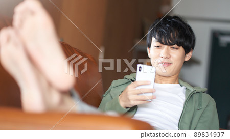 一個年輕人靠在沙發上，看著他的智能手機 89834937