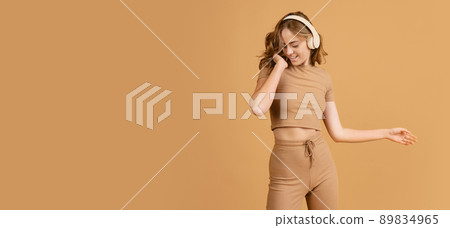 Happy girl, student listening to music and dancing isolated over brown color background. Concept of beauty, art, fashion, youth, monochrome Happy girl, student listening to music and dancing isolated over brown color background. Concept of beauty, art, fashion, youth, monochrome 89834965