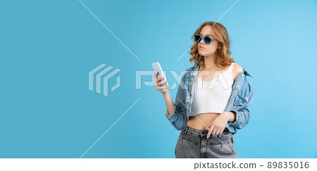 Young beautiful girl in casual style outfit using phone isolated on blue background. Concept of beauty, art, fashion, youth, fall collection Young beautiful girl in casual style outfit using phone isolated on blue background. Concept of beauty, art, fashion, youth, fall collection 89835016