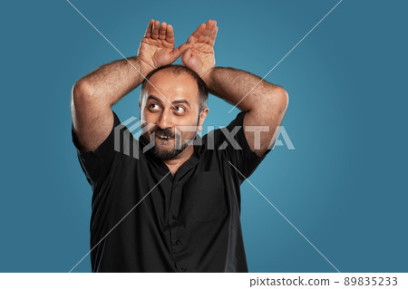 Close-up portrait of a brunet middle-aged man with beard, dressed in a black t-shirt and posing against a blue background. Close-up portrait of a brunet middle-aged man with beard, dressed in a black t-shirt and posing against a blue background. 89835233