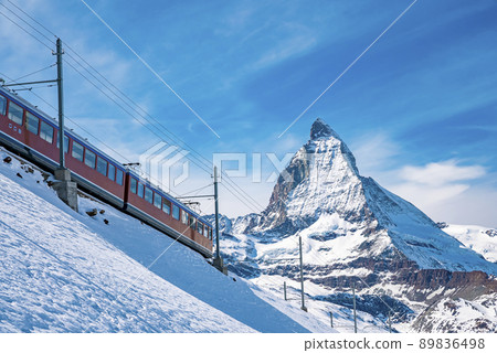 Train passing through snowcapped Matterhorn against blue sky 89836498