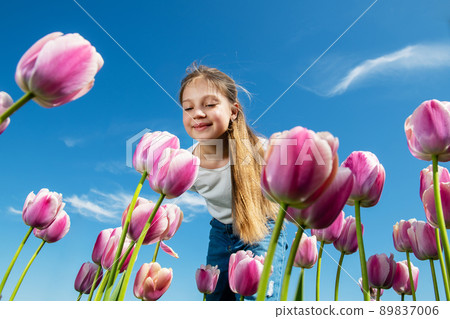 Bottom view of a girl looking at a tulip flower with sky background. 89837006