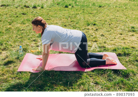 Healthy redhead woman wearing sportswear on pink mat practicing yoga, Donkey Kicks exercise on nature background. Sport, healthy life or yoga concept 89837093