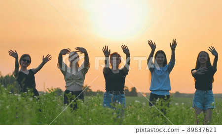 Girls friends waving their hands to the setting sun on the background of the sunset. Girls friends waving their hands to the setting sun on the background of the sunset. 89837621