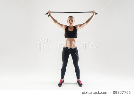 Trx equipment. Strong woman holding jumping rope near head and looking at camera. Studio shot, gray background 89837795