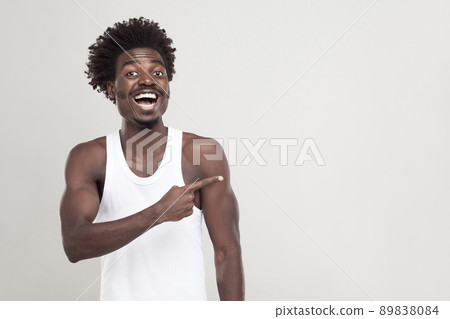 Man in white t-shirt showing finger at copy space. Studio shot. Gray background 89838084