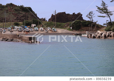 A landscape with a blue sky, a harbor with many fishing boats, a blue sea surface, rocks and trees 89838239