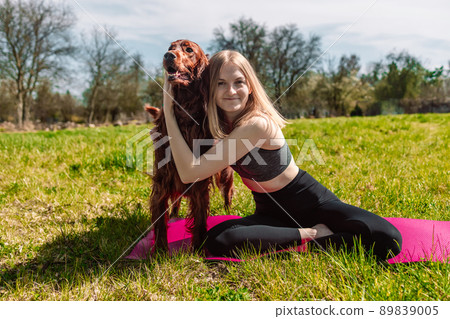 Cute young caucasian woman is meditating while sitting on a rug on the lawn on a sunny summer with Irish Setter dog. Cute young caucasian woman is meditating while sitting on a rug on the lawn on a sunny summer with Irish Setter dog. 89839005