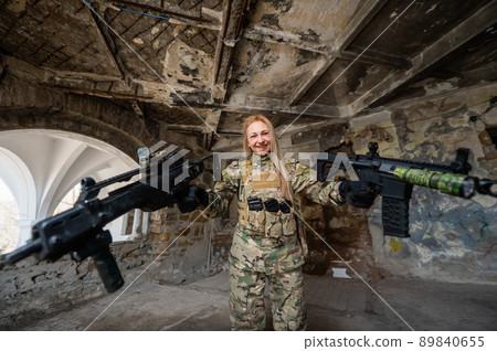 Caucasian woman in army uniform holding two machine guns.  89840655