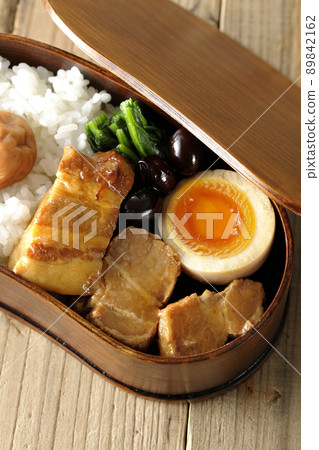 A bird's-eye view of a kakuni bento box containing black beans, spinach, and soft-boiled eggs in a bento 89842162