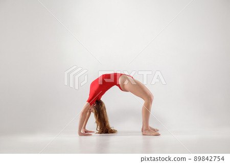 sporty woman balancing on hands and knees and holding back in form of arch while doing bridge urdhva dhanurasana yoga pose. indoor, light gray background. healthy lifestyle and leisure activity. 89842754