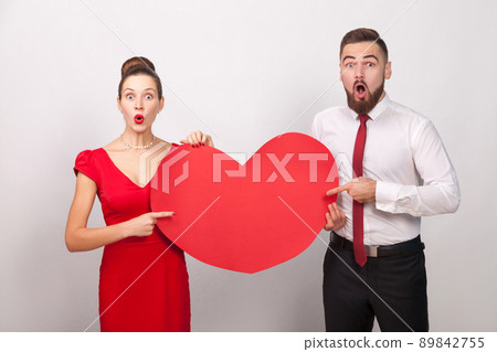 Wow! Big love. Wondered couple pointing fingers at red heard. Indoor, studio shot, isolated on gray background Wow! Big love. Wondered couple pointing fingers at red heard. Indoor, studio shot, isolated on gray background 89842755