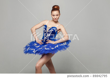 Portrait of beautiful happy ballerina woman in blue costume with makeup and bun collected hair standing against gray background, looking at camera. emotion and expression concept. indoor studio shot. Portrait of beautiful happy ballerina woman in blue costume with makeup and bun collected hair standing against gray background, looking at camera. emotion and expression concept. indoor studio shot. 89842795