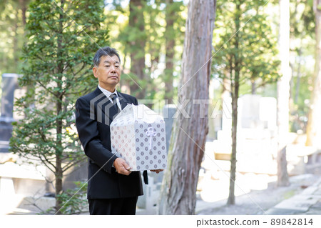 A man in mourning dress (urn) performing a bone-laying ceremony at a grave 89842814