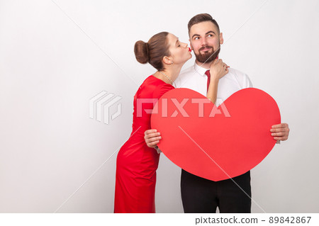 Man wish something, smiling, perfect woman kiss him at cheek. Indoor, studio shot, isolated on gray background 89842867