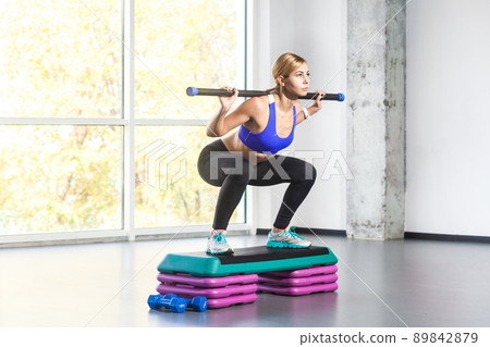 Blonde woman sit-ups, squad on step platform with barbell. Studio shot Blonde woman sit-ups, squad on step platform with barbell. Studio shot 89842879
