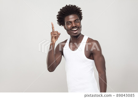 Good idea! Afro man finger up and toothy smiling. Indoor shot, gray wall Good idea! Afro man finger up and toothy smiling. Indoor shot, gray wall 89843085