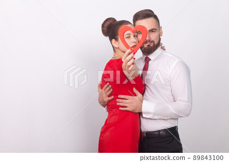 Beautiful couple embrace with passion, holding red heart. Indoor, studio shot, isolated on gray background 89843100