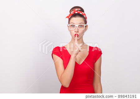Woman in red dress and dots bandsge, showing secret sign. Indoor, studio shot, isolated on gray background 89843191