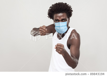 Portrait of angry young man wearing white shirt with surgical medical mask standing with boxing fists and ready to attack or defence. indoor studio shot isolated on gray background. 89843194