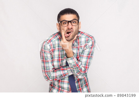 Portrait of сrazy shocked bearded businessman in colorful checkered shirt, blue tie and eyeglasses standing touching face and looking at camera. indoor studio shot, isolated on light grey background. Portrait of сrazy shocked bearded businessman in colorful checkered shirt, blue tie and eyeglasses standing touching face and looking at camera. indoor studio shot, isolated on light grey background. 89843199