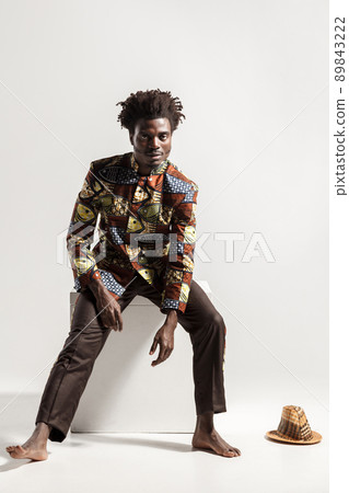 Afro man in national kongo national costume sit on cube . Indoor, isolated on gray background Afro man in national kongo national costume sit on cube . Indoor, isolated on gray background 89843222