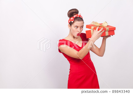 Cunning woman, looking inside gift box . Indoor, studio shot, isolated on gray background Cunning woman, looking inside gift box . Indoor, studio shot, isolated on gray background 89843340