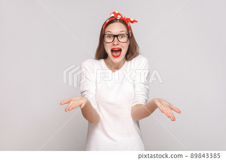 how you did this? it's unbelievable. portrait of beautiful emotional young woman in white t-shirt with freckles, black glasses, red lips and head band. indoor shot, isolated on light gray background. how you did this? it's unbelievable. portrait of beautiful emotional young woman in white t-shirt with freckles, black glasses, red lips and head band. indoor shot, isolated on light gray background. 89843385