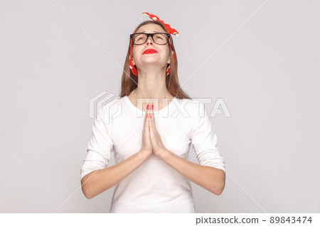 Oh my God please help me. portrait of beautiful emotional young woman in white t-shirt with freckles, black glasses, red lips and head band. indoor studio shot, isolated on light gray background. Oh my God please help me. portrait of beautiful emotional young woman in white t-shirt with freckles, black glasses, red lips and head band. indoor studio shot, isolated on light gray background. 89843474