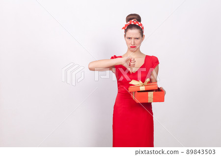 Dislike. Woman holding red box and demonstrate thumb down. Indoor, studio shot, isolated on gray background 89843503