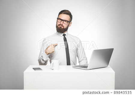 Portrait of satisfied confident smiling bearded young manager in white shirt and black tie are sitting in office are prouded of himself for achieved goals in work. Studio shot, indoor, isolated Portrait of satisfied confident smiling bearded young manager in white shirt and black tie are sitting in office are prouded of himself for achieved goals in work. Studio shot, indoor, isolated 89843535