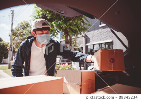 Asian postman with a hygiene protective face mask picking up a parcel package or parcel box from the truck for deliver to customer's door. New Normal concept during covid-19 or coronavirus pandemic Asian postman with a hygiene protective face mask picking up a parcel package or parcel box from the truck for deliver to customer's door. New Normal concept during covid-19 or coronavirus pandemic 89845234