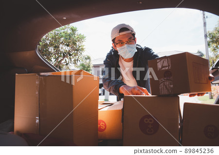 Asian postman with a hygiene protective face mask picking up a parcel package or parcel box from the truck for deliver to customer's door. New Normal concept during covid-19 or coronavirus pandemic Asian postman with a hygiene protective face mask picking up a parcel package or parcel box from the truck for deliver to customer's door. New Normal concept during covid-19 or coronavirus pandemic 89845236