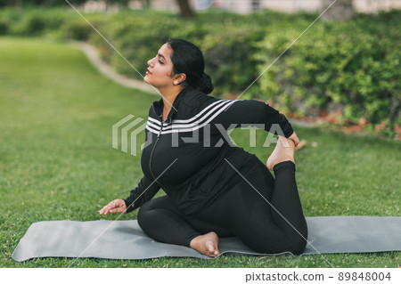An Indian girl practices yoga in a summer park in the afternoon, resting after a hard day. Practice, yoga, fitness 89848004