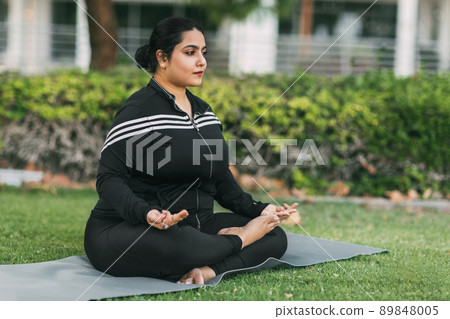 An Indian woman practices yoga and meditation in the lotus asana pose in an outdoor summer park. Side view. 89848005