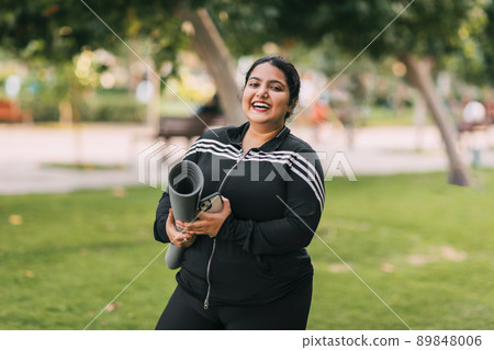 A young Indian woman holding a yoga mat returns after doing yoga or fitness outdoors A young Indian woman holding a yoga mat returns after doing yoga or fitness outdoors 89848006