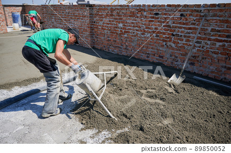 Male worker using concrete screed mixer machine while preparing sand-cement mix for floor screed. Man builder working with professional floor screed equipment at construction site. 89850052