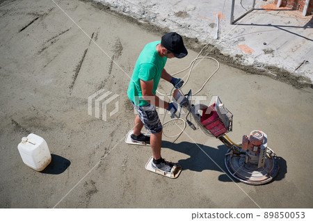 Aerial view of man builder using troweling machine while screeding floor. Worker finishing concrete surface with floor screed grinder machine at construction site on the roof of residential building. 89850053