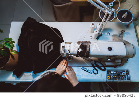A woman tailor sews clothes - a fashionable jacket made of velvet fabric on a sewing machine in her atelier 89850425
