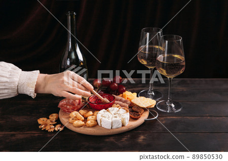 Woman's hand takes a piece of cheese from the Appetizers board with assorted cheese, meat, sausage rosette, grape and cookies 89850530