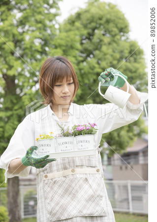 A woman in gardening working watering a flower in a planter 89852006
