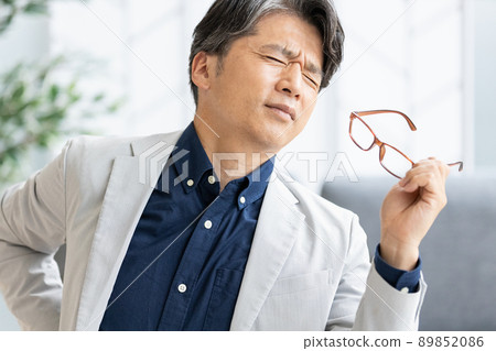 An unwell man who puts his hand on his back during desk work 89852086